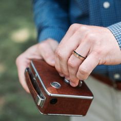 a man wearing a wedding band holding an old fashioned camera with his hand on it