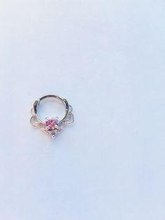 a ring with a pink stone on it sitting on top of a white table next to a pair of scissors