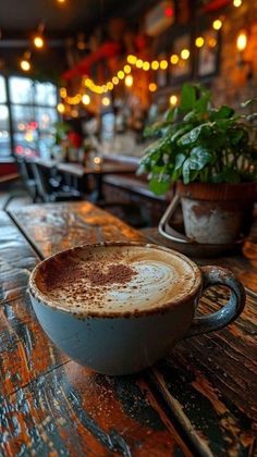 a cup of coffee sitting on top of a wooden table next to a potted plant