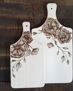 two wooden cutting boards with floral designs on them, one is white and the other is brown