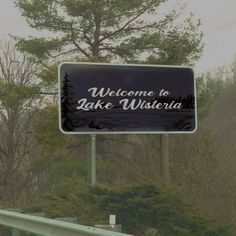 a welcome to lake wisteria sign on the side of a road with trees in the background