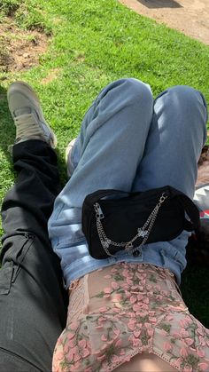 two people laying on the grass with their legs crossed and one holding a black purse