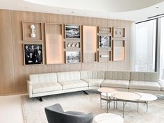 a living room filled with white furniture next to a large glass window covered in framed pictures