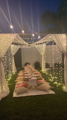 a long table covered with pillows and lights in the middle of an outdoor area at night