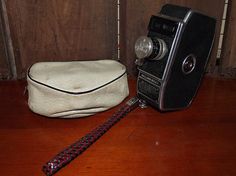 an old fashioned camera sitting on top of a wooden floor next to a white bag