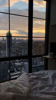 a bed sitting next to a window in a bedroom under a sky filled with clouds