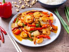 a white plate topped with shrimp and veggies next to chopsticks on a wooden table