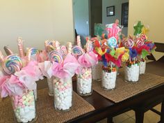 there are many candy in glass jars on the table with pink bows and lollipops