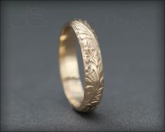 a gold wedding ring with an intricate design on the outside and inside, sitting on a gray surface