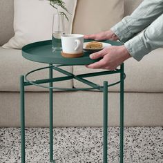 a person holding a coffee cup on top of a green table next to a couch