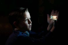 a young boy is holding his hand up in the air with light shining on him