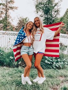 two young women standing in the grass with an american flag on their shoulders and arms