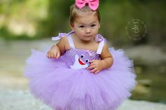 a baby girl wearing a purple tutu with a pink bow on her head and holding a stuffed animal