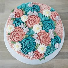 a cake decorated with pink, blue and white frosting flowers on top of a wooden table