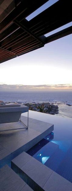 an outdoor swimming pool next to a large body of water at dusk with the ocean in the background