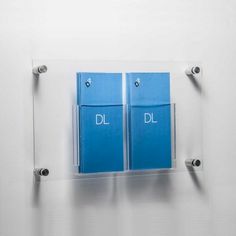 two blue folders are attached to a clear glass holder on a white wall,