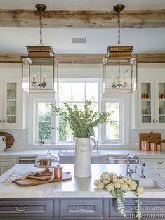 a kitchen with white cabinets and an island in front of a window that has hanging lights above it