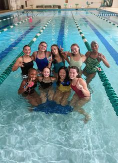 a group of women standing in a swimming pool posing for a photo with their arms around each other