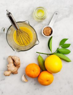 oranges, ginger and other ingredients on a marble counter top with whisk