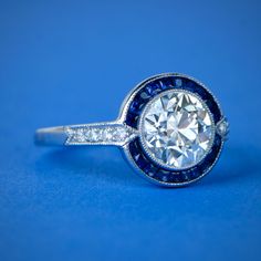 a diamond and blue sapphire ring on a blue background with the center stone surrounded by diamonds