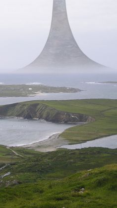 a large mountain towering over a lake surrounded by lush green fields and grass covered hills