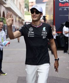 a man in black shirt and white pants walking down the street with his hand up