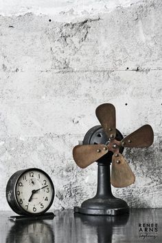 an old fashioned clock sitting on top of a table next to a wall mounted fan