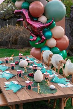 an outdoor party with balloons, plates and decorations on a wooden table in the grass