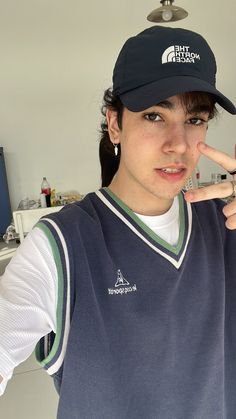 a young man in a baseball cap making the peace sign with his hand while standing in front of a computer screen