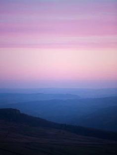 the sky is pink and purple as it rises above the hills in the distance,