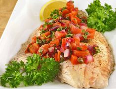 a white plate topped with fish covered in veggies and garnishes