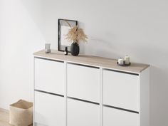 a white cabinet with two candles and a vase on top, next to a wicker basket