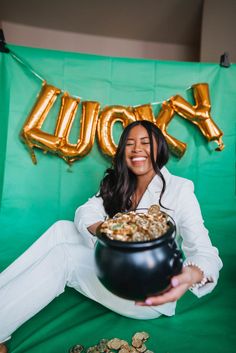 a woman sitting on the floor holding a caulder full of gold coins in front of a green backdrop