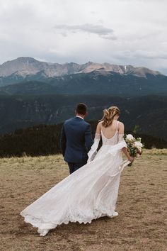 the bride and groom are walking towards the mountains in their wedding dress, which is adorned with lace