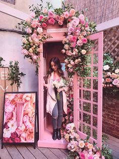 a woman standing in a pink phone booth surrounded by flowers