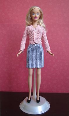 a barbie doll wearing a pink sweater and blue skirt with black heels standing on a white pedestal