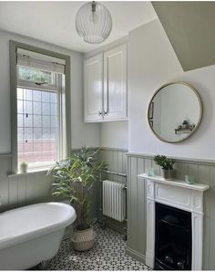 a white bath tub sitting next to a fireplace in a bathroom under a mirror above a window