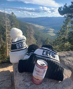 two hats and a can of beer sitting on top of a rock in the mountains