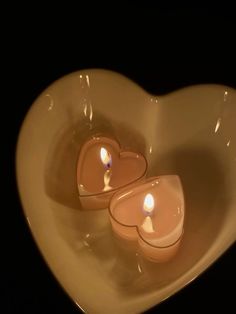 two candles in the shape of a heart on top of a white bowl with black background