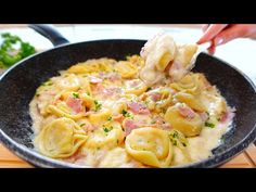 a person is spooning some pasta with ham and cheese in a skillet on a wooden table