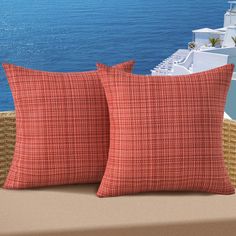 two red pillows sitting on top of a couch next to the ocean