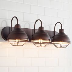 three lights are hanging on the wall next to a white brick wall in a bathroom