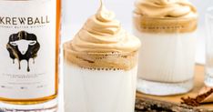 two glasses filled with whipped cream next to a bottle of booze and cinnamon sticks