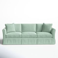 a light green couch with four pillows on the back and one arm folded over it, sitting in front of a white wall