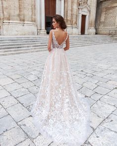 a woman standing in front of a building wearing a wedding dress with an open back