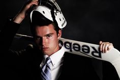 a man in a suit and tie holding a hockey helmet on top of his head