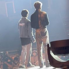 two young men standing on stage in front of an audience with their backs to the camera