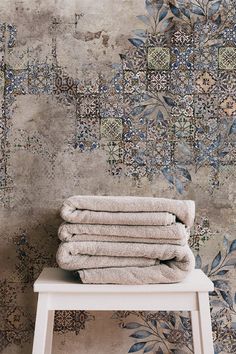 stack of towels sitting on top of a white stool in front of a floral wallpaper