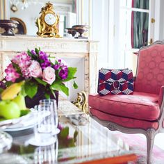 a red chair sitting in front of a fireplace next to a vase filled with flowers