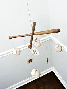 a baseball themed mobile hangs in the corner of a room with white walls and wood flooring